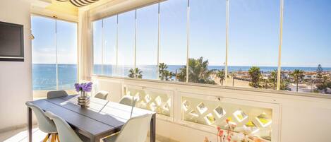 Un comedor con vista al mar, una mesa con sillas y un jarrón con flores.