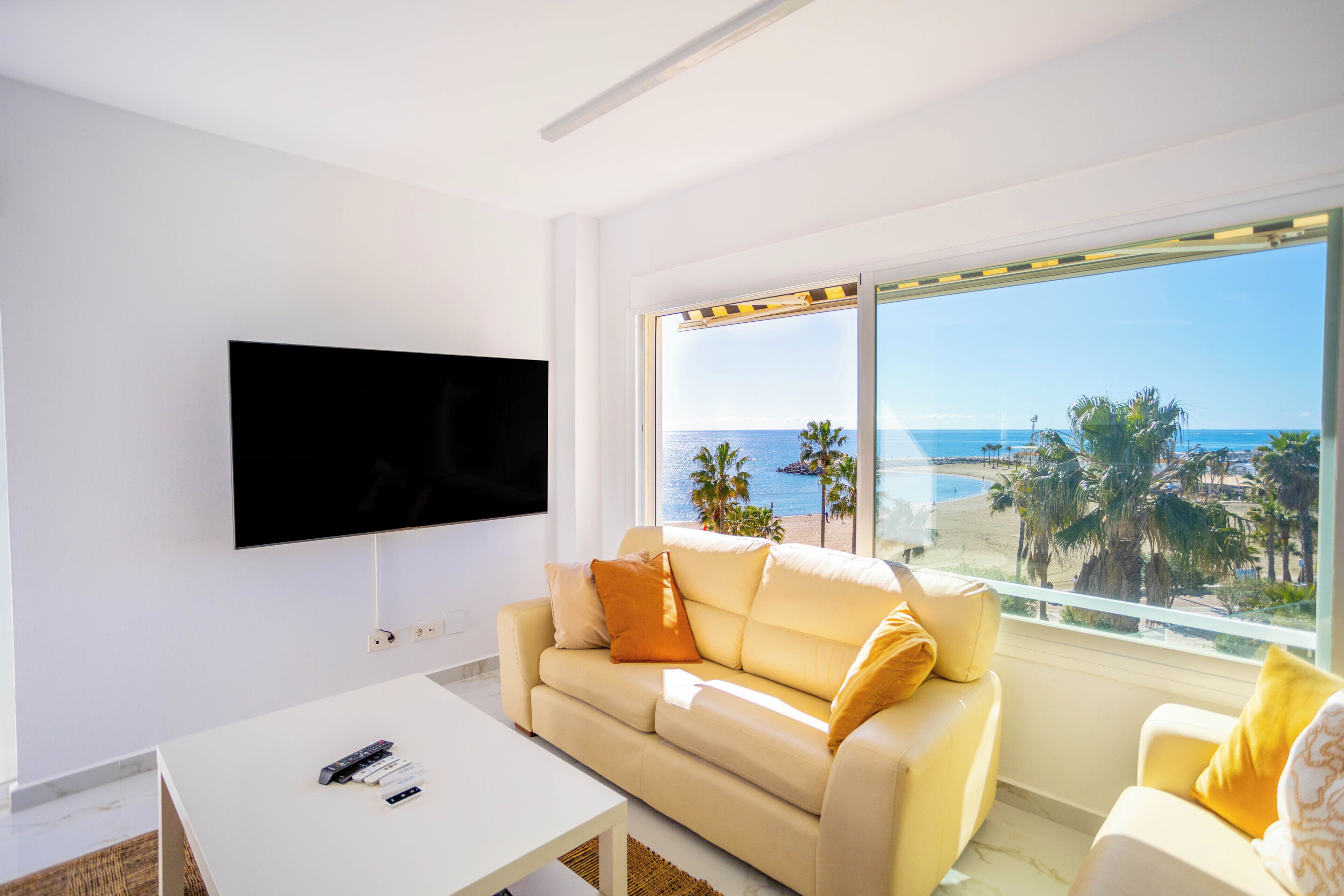 A modern living room with a flat-screen TV, a beige sofa, and a white coffee table.
