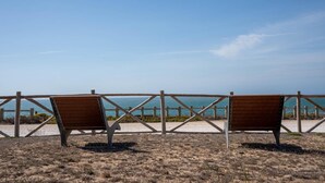 Zwei hölzerne Bänke, die auf einen Strand mit Holzzaun und einem klaren Himmel blicken.