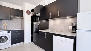 Una cocina moderna con armarios oscuros, horno empotrado, lavavajillas y cafetera.