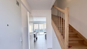 Un interior moderno con una escalera, una puerta con un número y vistas a un comedor.