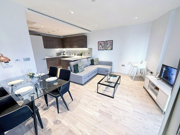 Eine moderne Wohnung mit Essbereich, Wohnzimmer mit Sofa und Couchtisch, Küche und Fernseher.