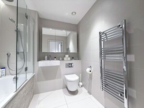 Ein modernes Badezimmer mit Duschkabine aus Glas, Toilette in Weiß, Waschbecken mit Spiegel und Handtuchhalter.