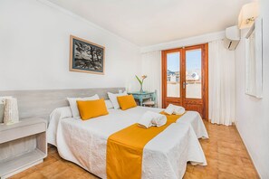A hotel room with a bed, a desk, a chair, a window with curtains, and a painting on the wall. - Atico - Penthouse Bressol (Port de Pollença)