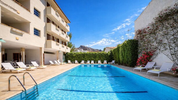 A swimming pool with lounge chairs, a building with balconies, and a clear sky. - Apartment 2C - Penthouse Bressol (Port de Pollença)
