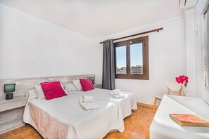 Ein Hotelzimmer mit zwei Betten, einem Schreibtisch, einem Stuhl, einem Fenster mit Vorhängen und Blick auf Gebäude.