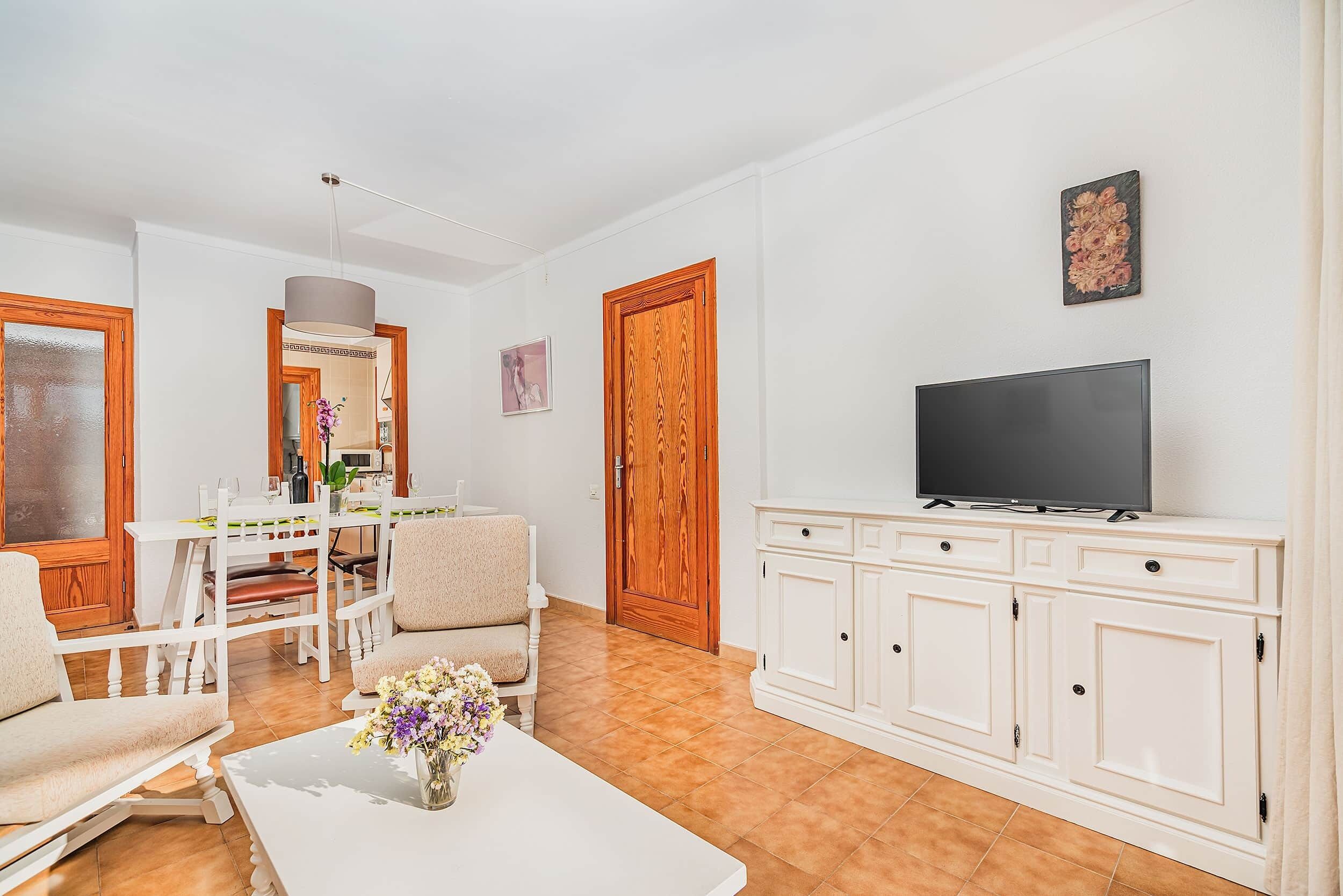 A living room with a TV, white furniture, a dining table, and a wooden door.