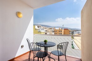 Un balcon avec une table ronde, deux chaises, une petite plante en pot et une vue sur des immeubles et des montagnes.