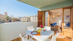Uma varanda com mesa posta para refeições, uma cadeira e vista para a cidade.