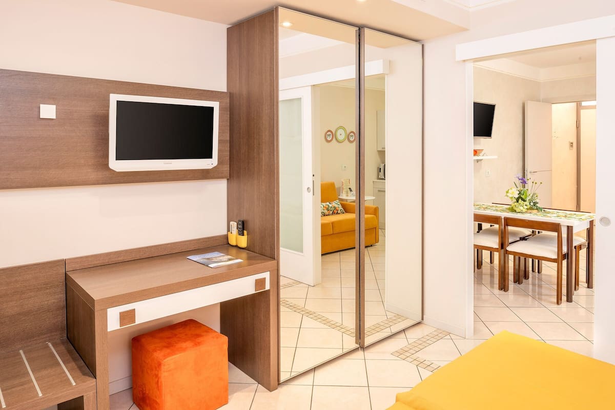 A modern room with a desk, a television, a sliding door, and a dining area with a table and chairs.