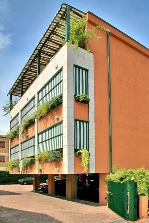 A multi-story building with a flat roof, vertical garden installations, and a brick-paved entrance area.