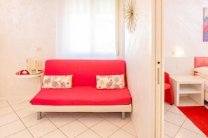 A room with a red sofa, a small white side table, a white chair, and a red rug.