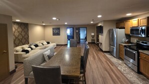Una cocina moderna con electrodomésticos de acero inoxidable, un comedor con mesa de madera y una sala de estar con sofá y cojines estampados.