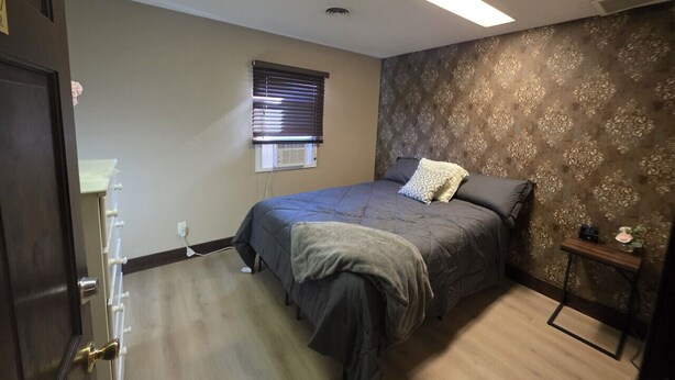 Un dormitorio con cama, ventana con persianas, radiador y una mesita de noche con planta.