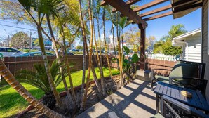 A covered patio with a table and chairs, surrounded by palm trees and a view of a street with parked cars.