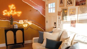 Uma sala de estar com um sofá, uma mesinha lateral, um letreiro de neon e obras de arte nas paredes.