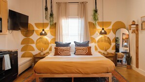 Quarto com cama, mesas de cabeceira, televisão e uma janela grande com cortinas.