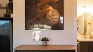 Uma cozinha com mesa de madeira, dois banquinhos, uma planta em vaso e um quadro grande na parede.