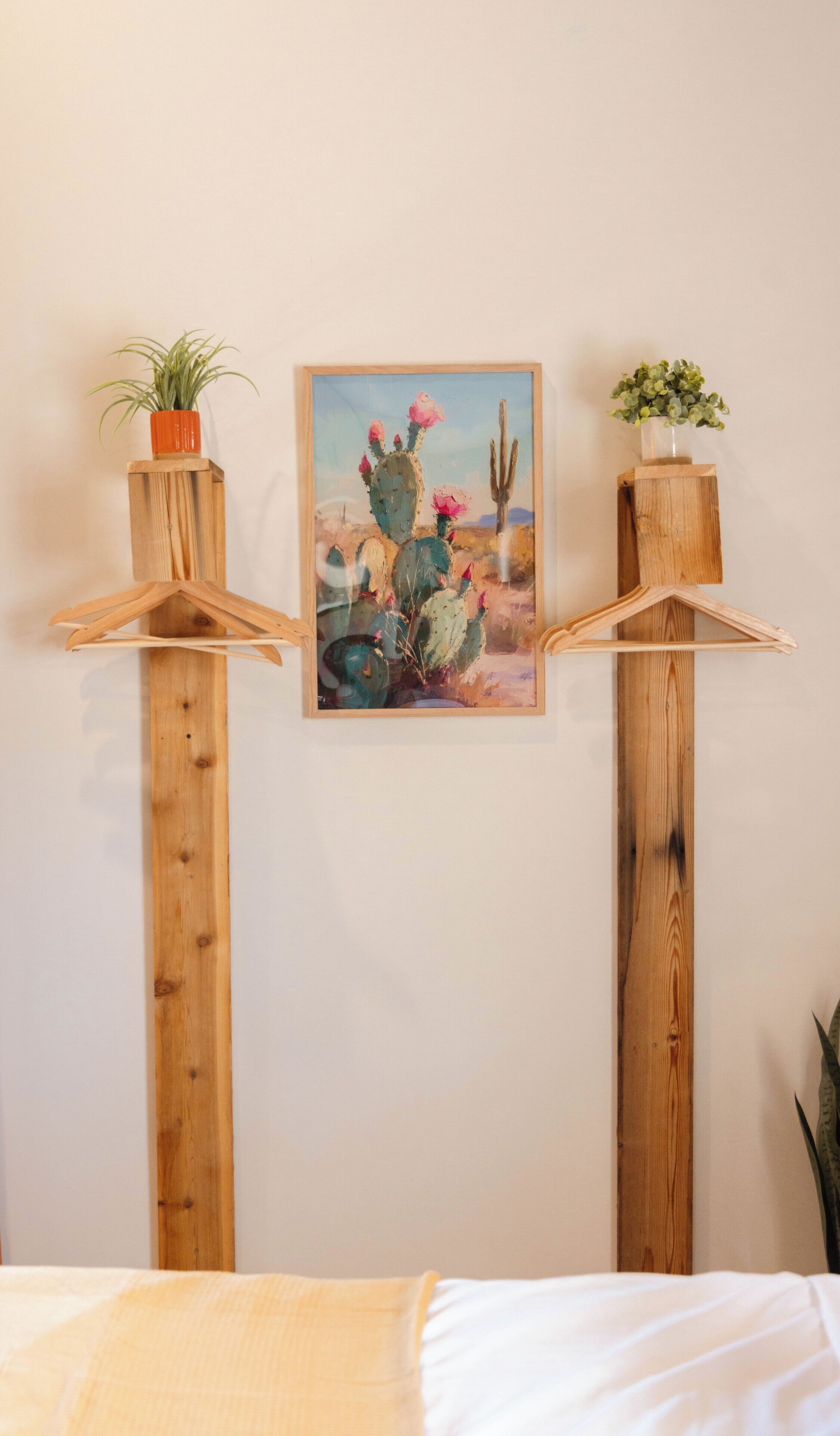 A bedroom with a bed, a wooden shelf with a cactus painting, and a potted plant.
