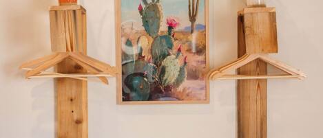 A bedroom with a bed, a wooden shelf with a cactus painting, and a potted plant.