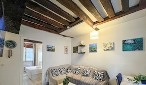 A room with a bed, a sofa with patterned cushions, a ceiling with exposed beams, and various wall art. - Urban Flat 192 - Charming flat - Basfour (París)