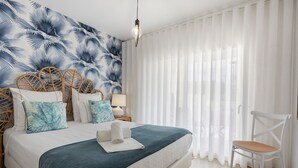 Une chambre à coucher comprenant un lit, une chaise, une table de chevet et un mur orné d’un motif de feuilles.