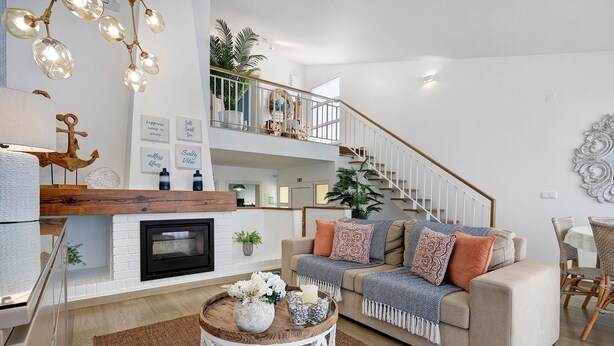 Un salon moderne avec une cheminée, une table basse ronde, un canapé agrémenté de coussins et un escalier menant à un niveau supérieur.