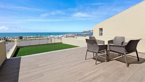 Un balcon avec vue sur la mer, deux fauteuils en osier et une petite portion de gazon artificiel.