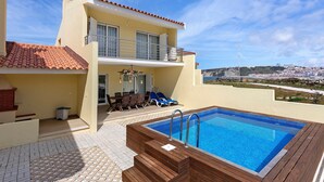 Un bâtiment à deux étages doté d’une piscine, d’un espace extérieur aménagé et offrant une vue sur une ville lointaine.