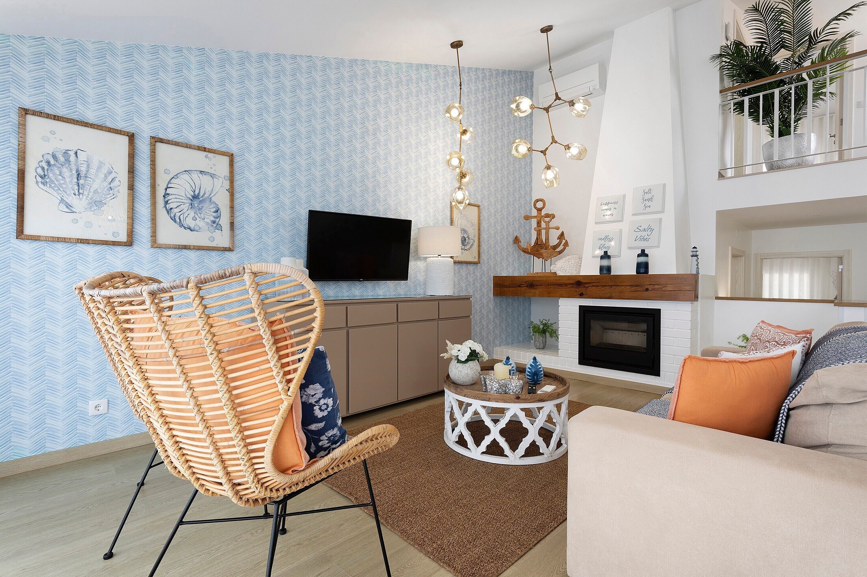 A living room with a television, a fireplace, a hanging light fixture, and a wicker chair.