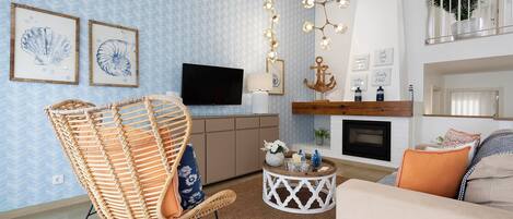 A living room with a television, a fireplace, a hanging light fixture, and a wicker chair.