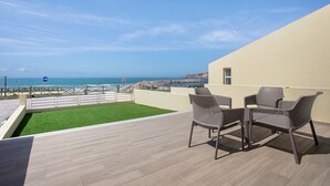 Une terrasse sur le toit offrant une vue sur la mer, deux fauteuils en osier et un petit coin de gazon artificiel.
