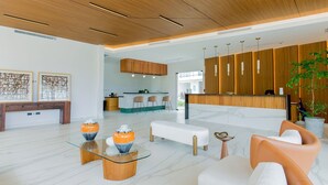 Uma área de recepção moderna com balcão de madeira, assentos e uma mesa de centro de vidro com vasos decorativos.