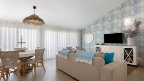 Een woonkamer met een bank, televisie en een eethoek met stoelen en een tafel.