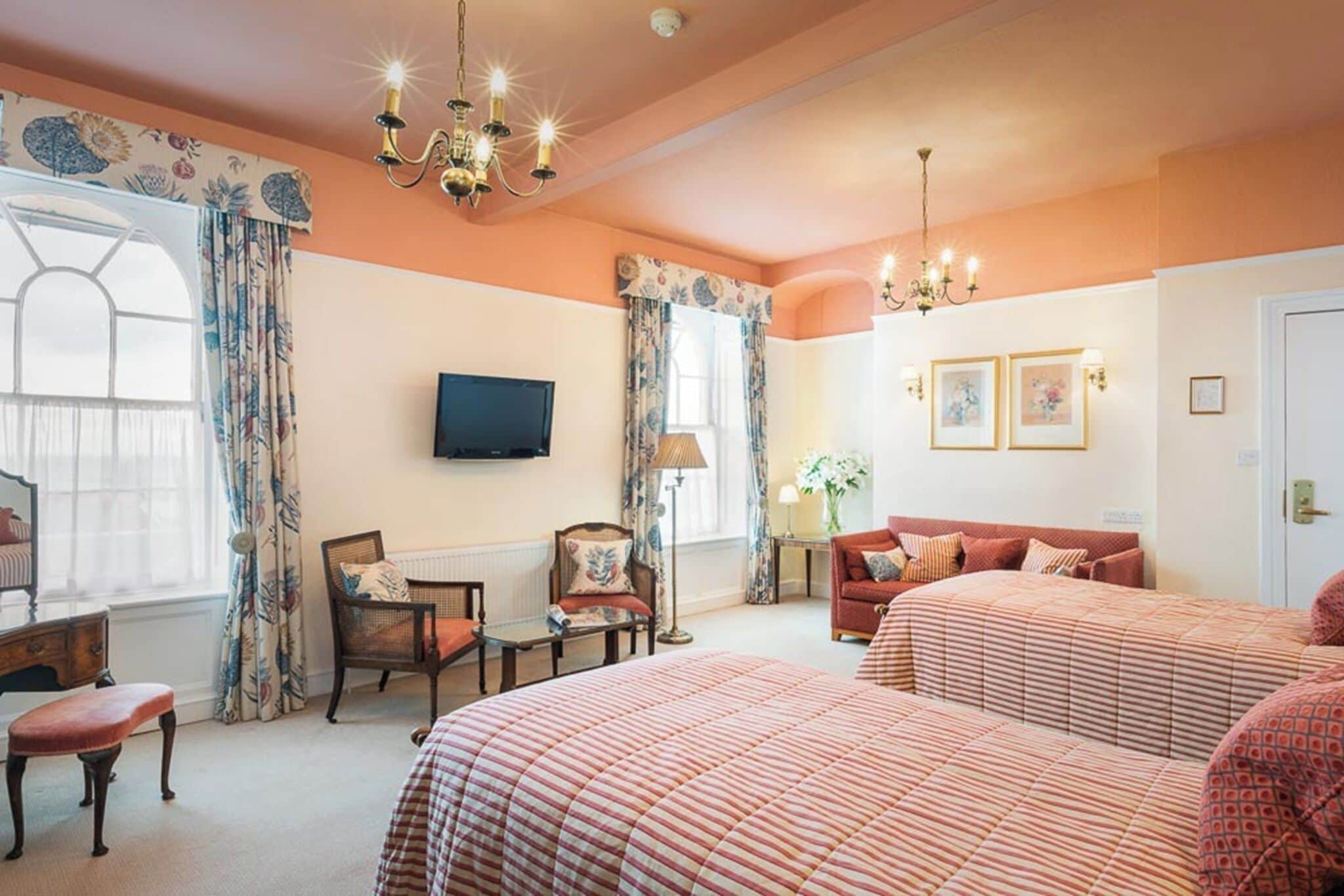 A hotel room with two beds, a television, a chandelier, and a window with curtains.