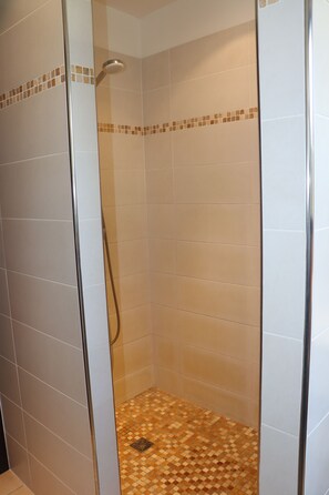 Eine gläserne Dusche mit gefliestem Boden und Wänden, einer Duschbrause und einem Abfluss.