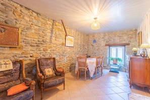 Une pièce aux murs de pierre, comprenant une table à manger, des chaises, un buffet en bois et un lustre.