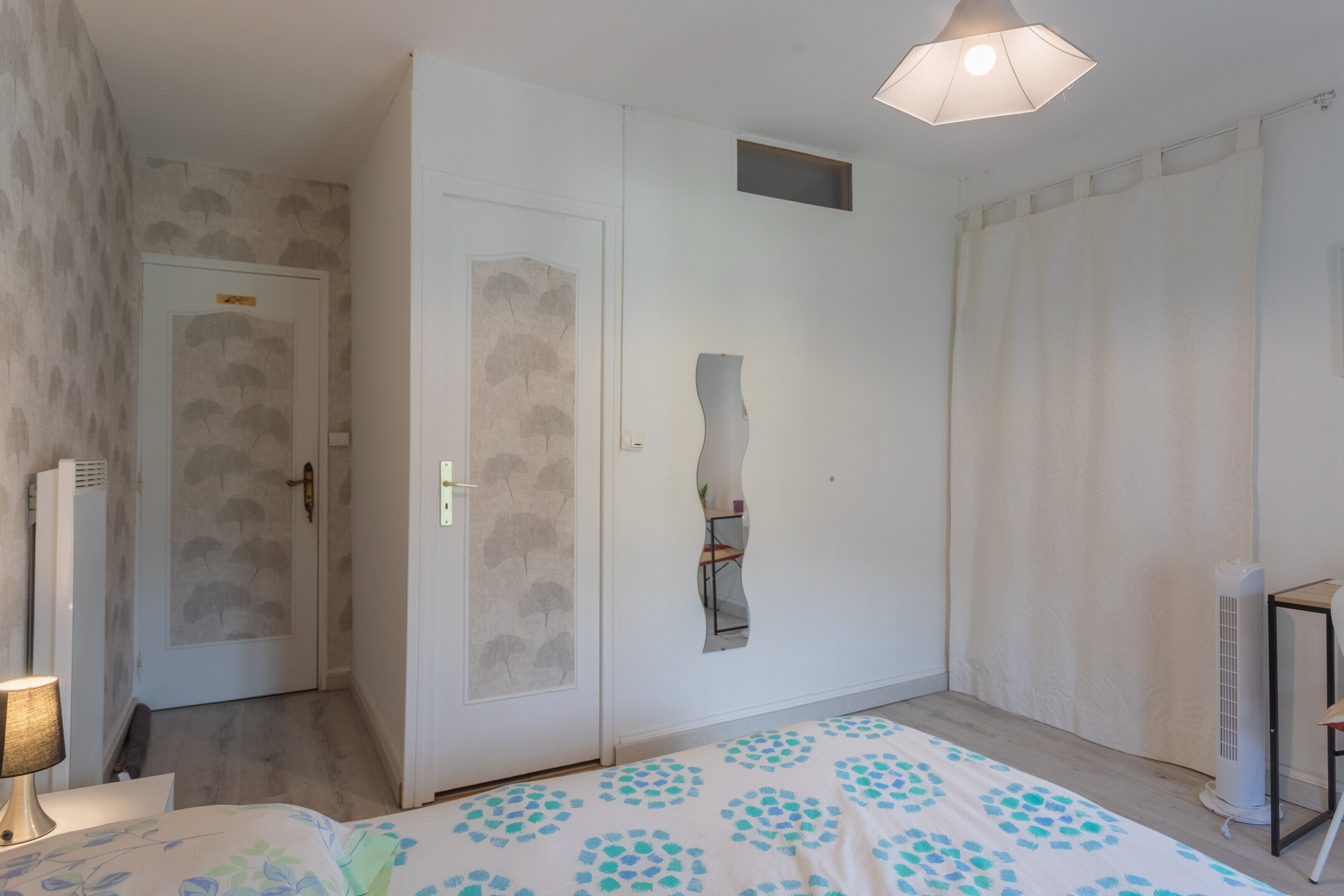 A bedroom with a bed, a bedside table, a lamp, a wardrobe, and a mirror.