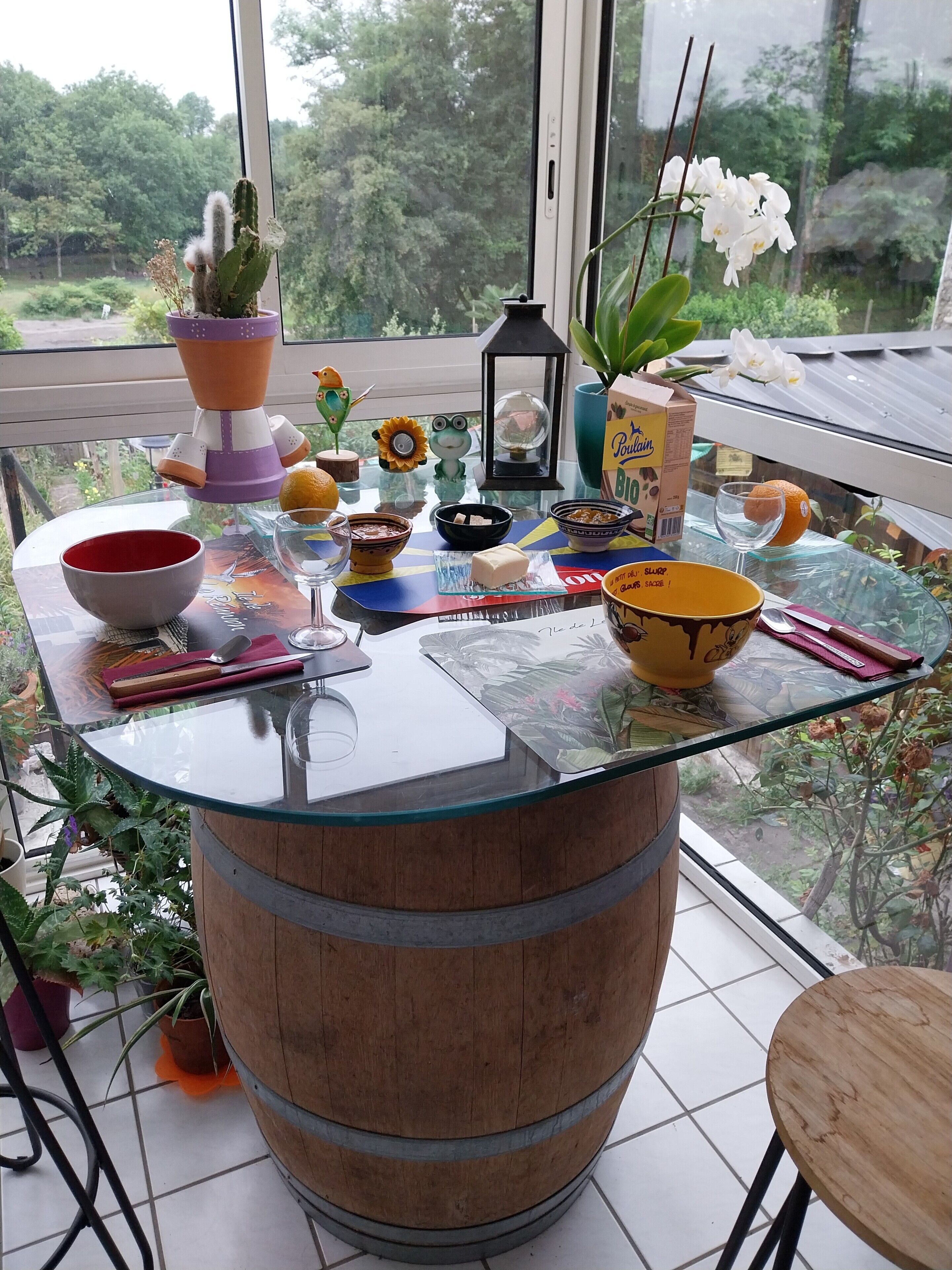Een tafel met glazen blad en een houten vatenvoet, omringd door diverse objecten, zoals een kom, kandelaar en een doos kaarsen.