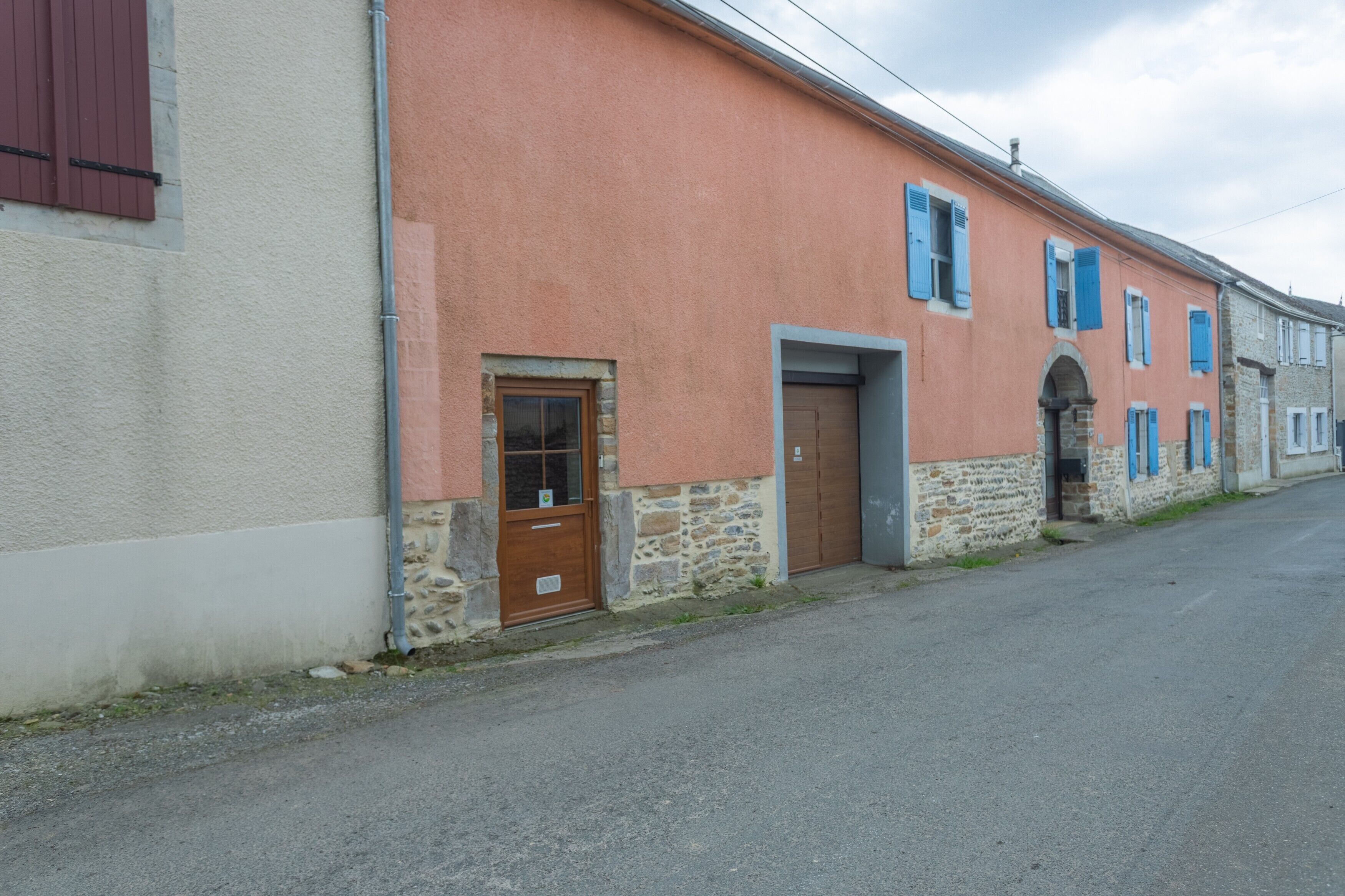 A building with a stone base and a pink upper wall, featuring a wooden door and blue shutters.