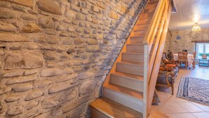 Un mur en pierre, un escalier en bois et un salon confortable avec des meubles.