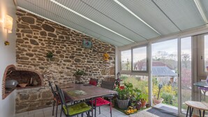 Un mur de pierres, un four en briques, une table à manger avec des chaises et des plantes en pot.