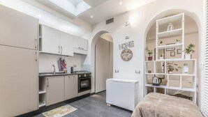A compact kitchen with modern appliances, a small refrigerator, and a cozy bed area with a shelf unit. - Battistini Sweet House (Roma)