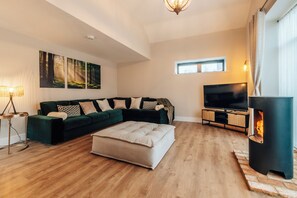 A living room with a sectional sofa, a flat-screen TV, a fireplace, and a large window. - The Stables (Huntingdon)