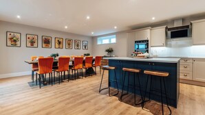 A modern kitchen with a dining area, wooden flooring, and bar stools. - The Stables (Huntingdon)