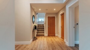 A hallway with wooden flooring, a staircase, and a door leading to another room. - The Stables (Huntingdon)