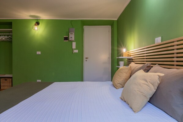 A bedroom with a bed, pillows, a bedside table, a lamp, a wardrobe, and a door. - The Green Attic by Wonderful Italy (Turin)