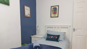 Ein Schlafzimmer mit einem Bett, einem Nachttisch, einer Lampe, einem gerahmten Bild an der Wand und einer Tür.