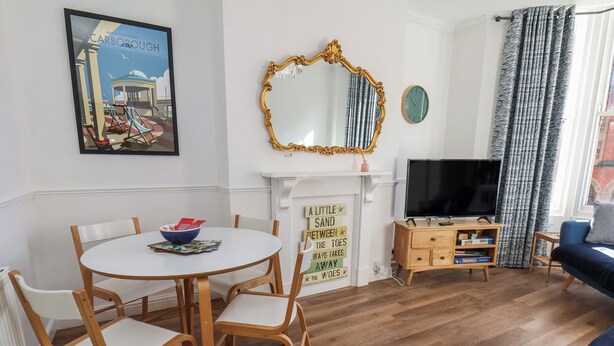 Ein Wohnzimmer mit rundem Esstisch, Holzstühlen, einem Fernseher, einem Kamin und einem blauen Sofa.