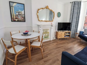 A living room with a round dining table, wooden chairs, a TV, a fireplace, and a blue sofa. - Granby Place Apartment 2 (Scarborough)